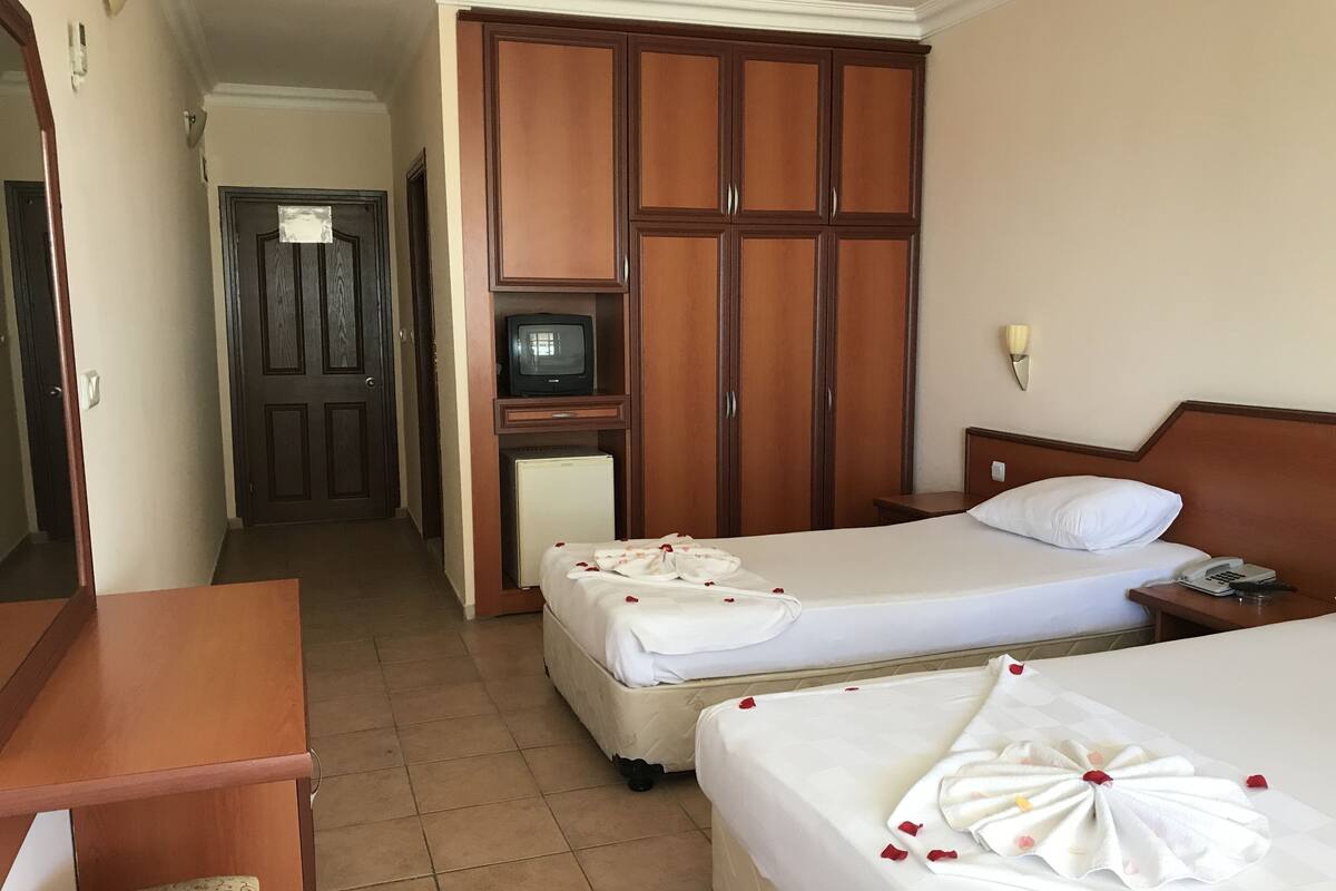 A hotel room with two beds, a desk, a wardrobe, and a television.
