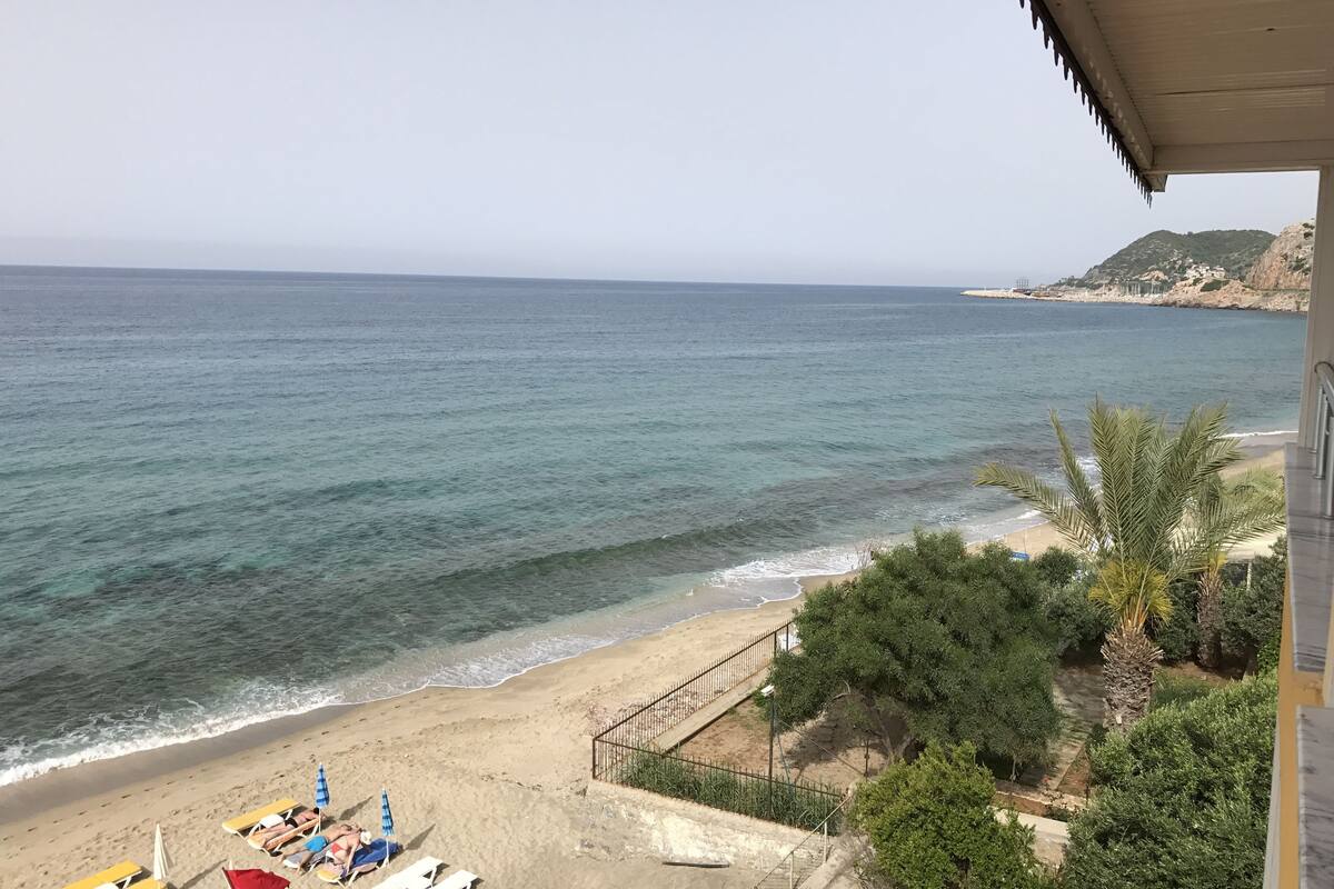 A beach view with a clear sky, a sandy shore, and a few people relaxing on sun loungers.