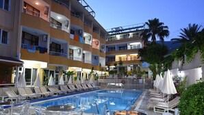 A hotel pool area with lounge chairs and tables, a multi-story building with balconies, and a clear sky. - Muz Hotel - All Inclusive (Alanya)
