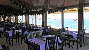 A restaurant with tables and chairs arranged for dining, large windows offering a view of the sea, and a wooden ceiling. - Muz Hotel - All Inclusive (Alanya)