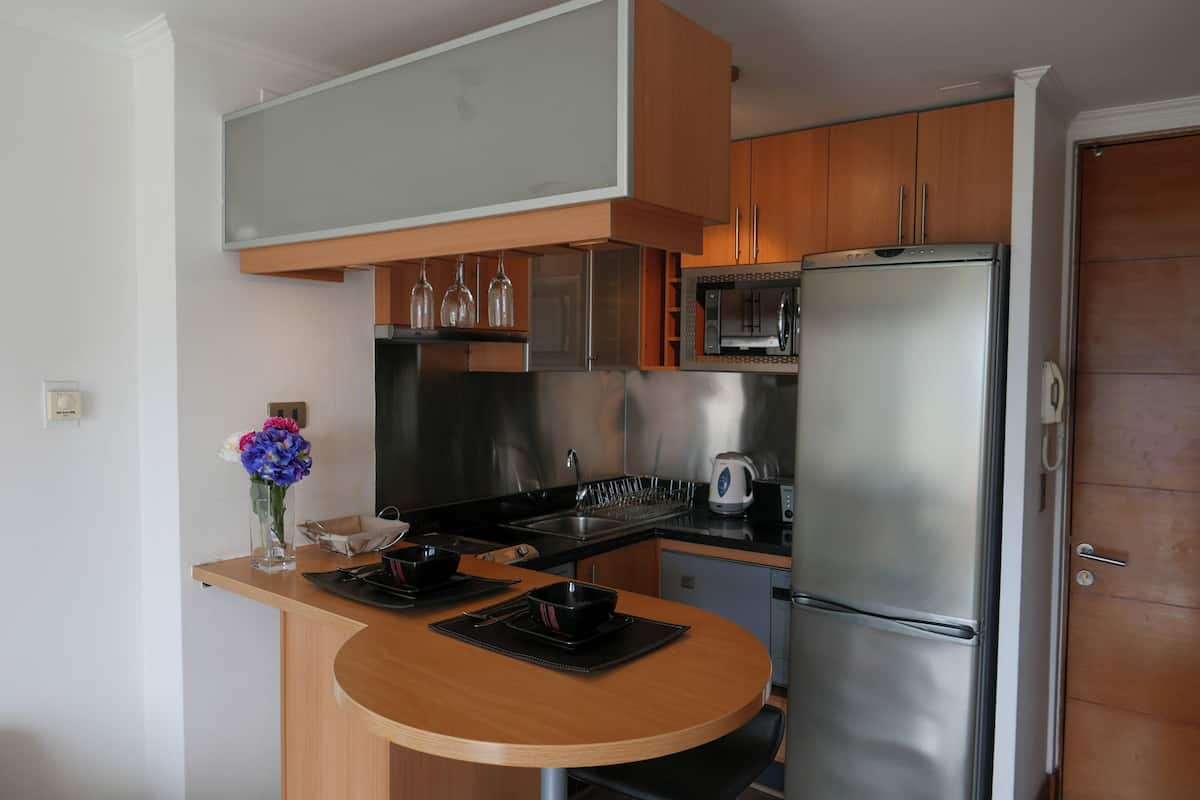 Cocina compacta equipada con microondas, refrigerador y un pequeño comedor con mesa y sillas de madera.