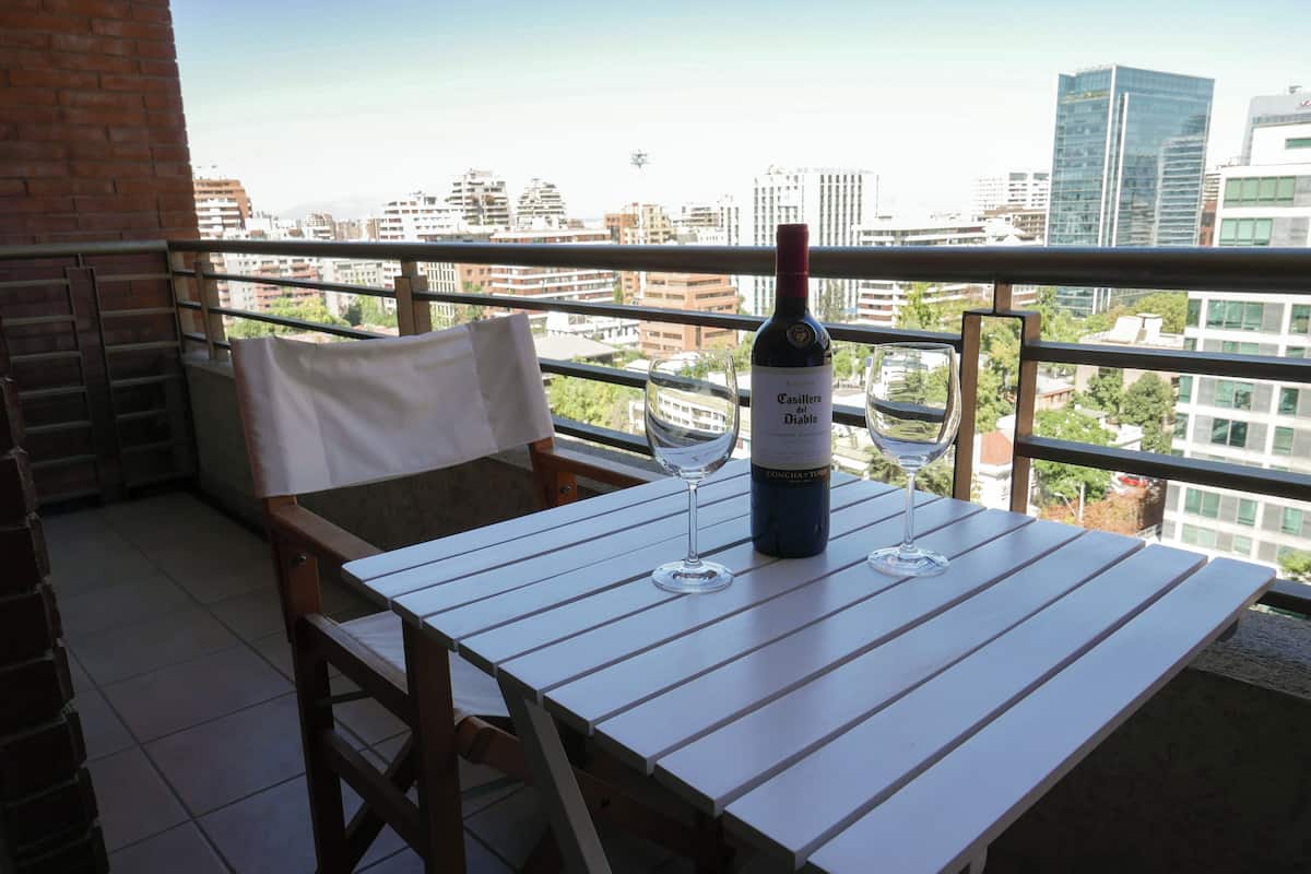 Un balcón con una mesa, dos copas de vino y una botella.