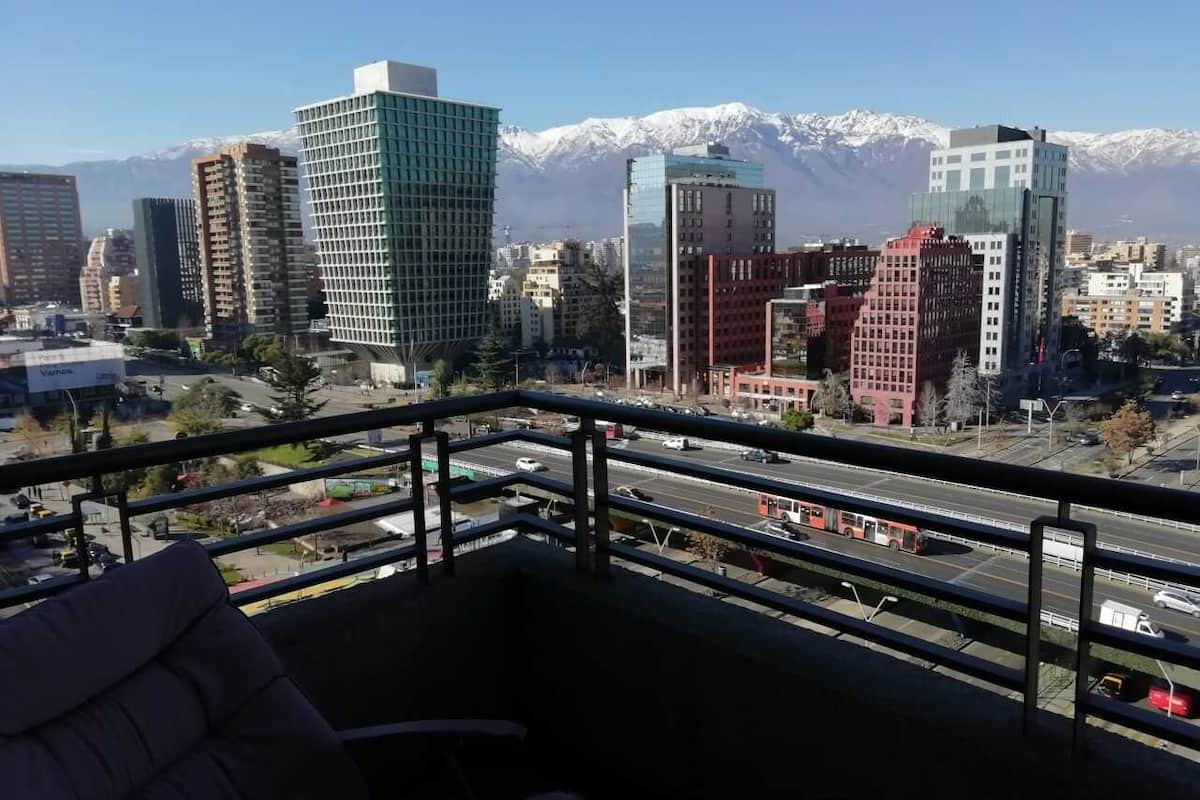 Un balcón con vistas a la ciudad, que incluye edificios modernos y una cadena montañosa al fondo.