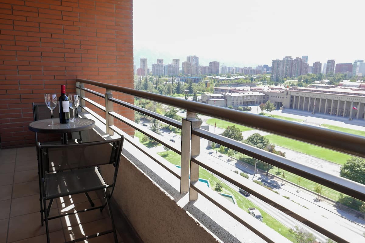 Un balcón con mesa y sillas, una botella de vino y vistas de un paisaje urbano con edificios y una carretera.