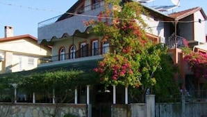 A two-story building with a balcony, a stone wall, and a garden with pink flowers. - Besik Hotel (Fethiye)