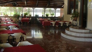 An indoor dining area with tables covered in red tablecloths, white chairs, and potted plants. - Besik Hotel (Fethiye)
