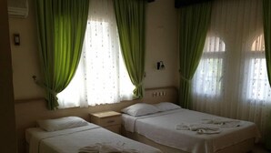A hotel room with two beds, a nightstand, and a TV. - Besik Hotel (Fethiye)
