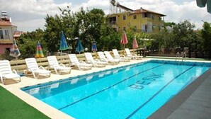 A swimming pool with lounge chairs and umbrellas, surrounded by greenery and buildings. - Besik Hotel (Fethiye)