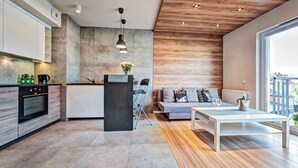 A modern kitchen with a central island, a dining area with a white table, and a living space with a sofa and cushions.
