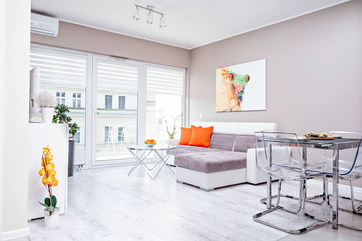 Un salon moderne avec un canapé, une table à manger en verre et une grande fenêtre équipée de stores.
