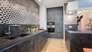 A modern kitchen with a black and white geometric backsplash, stainless steel appliances, and a wooden countertop.