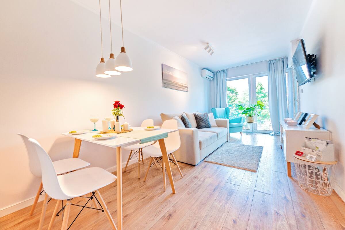 Un salon moderne comprenant un coin repas, un ensemble de canapés et un téléviseur fixé au mur.