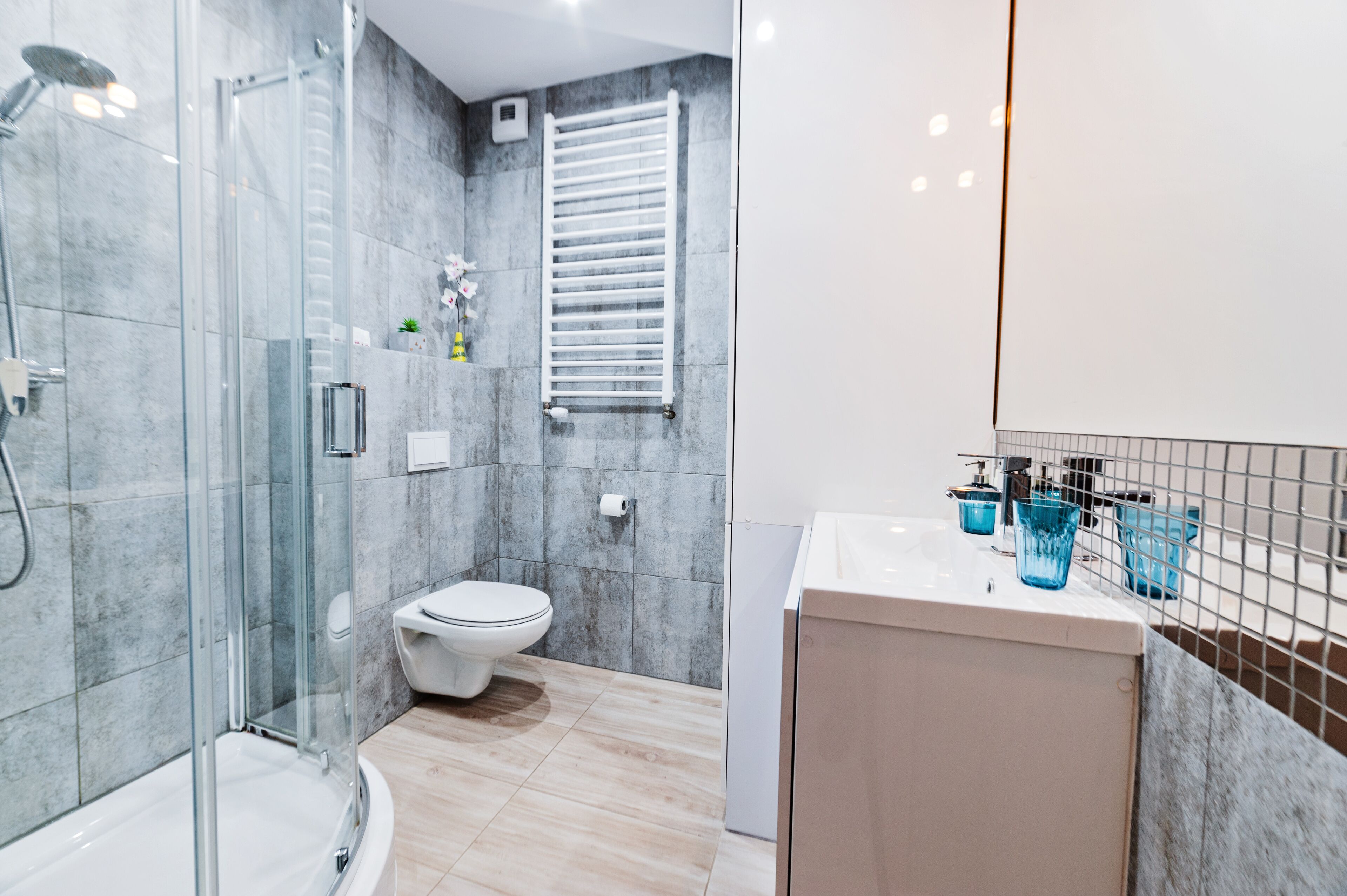 Un bany modern amb plat de dutxa envoltat de vidre, un vàter i un lavabo amb recipients de vidre blaus.
