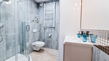 Un bany modern amb plat de dutxa envoltat de vidre, un vàter i un lavabo amb recipients de vidre blaus.