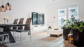 A modern living room with a dining area, a large flat-screen TV, and a view of the outside.