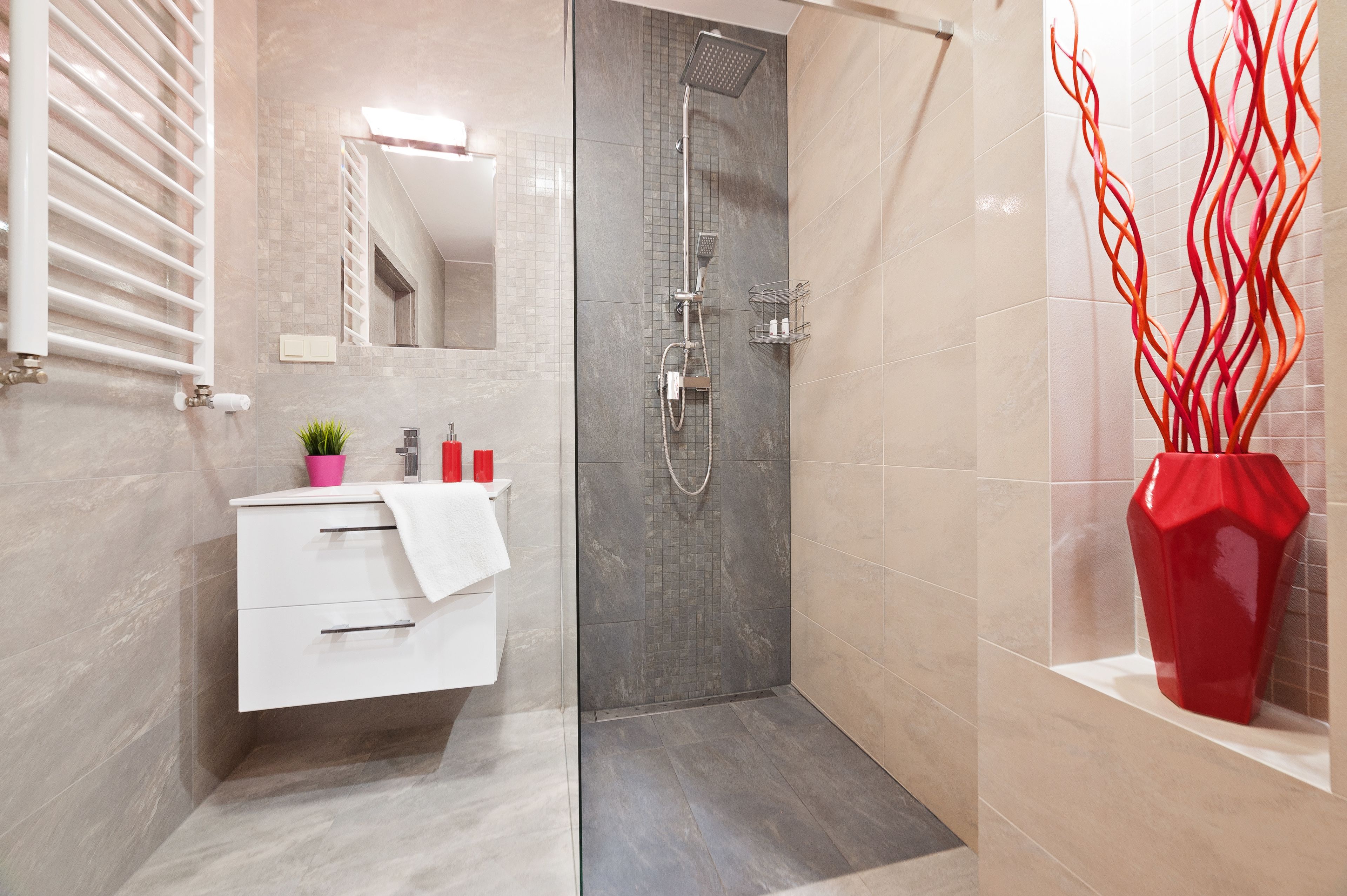 Een moderne badkamer met een douche, een witte wastafel met lades, een spiegel en een rode vaas.