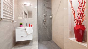 Een moderne badkamer met een douche, een witte wastafel met lades, een spiegel en een rode vaas.