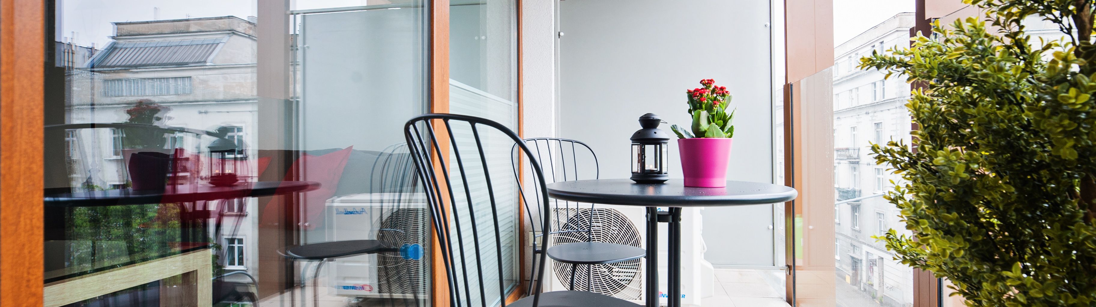 A balcony with a table, chairs, a potted plant, and a lantern.