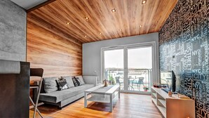 A modern living room with a grey sofa, a wooden ceiling, and a city-themed wall.