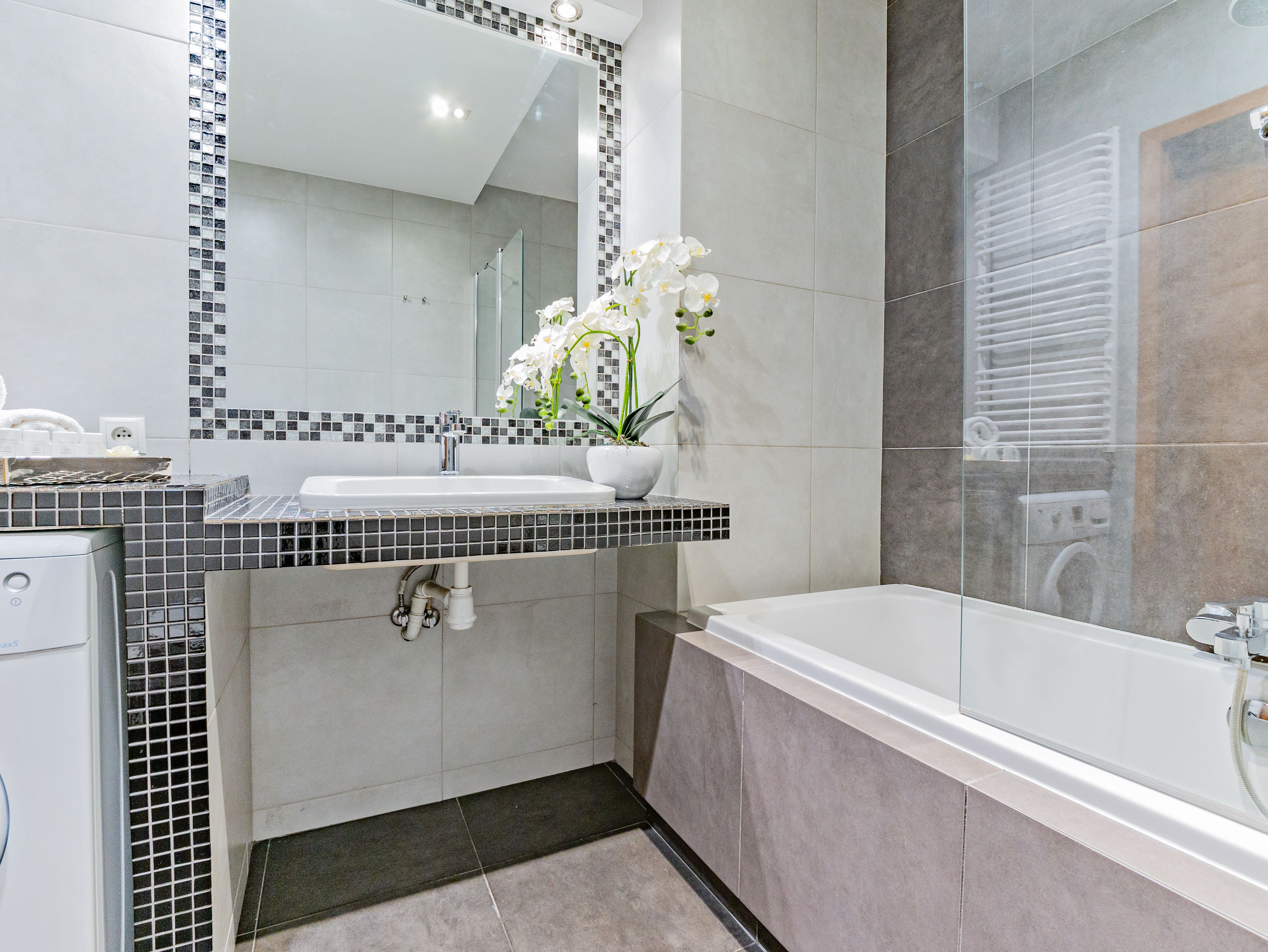 Un baño moderno con un espejo grande, un lavamanos blanco y una bañera.