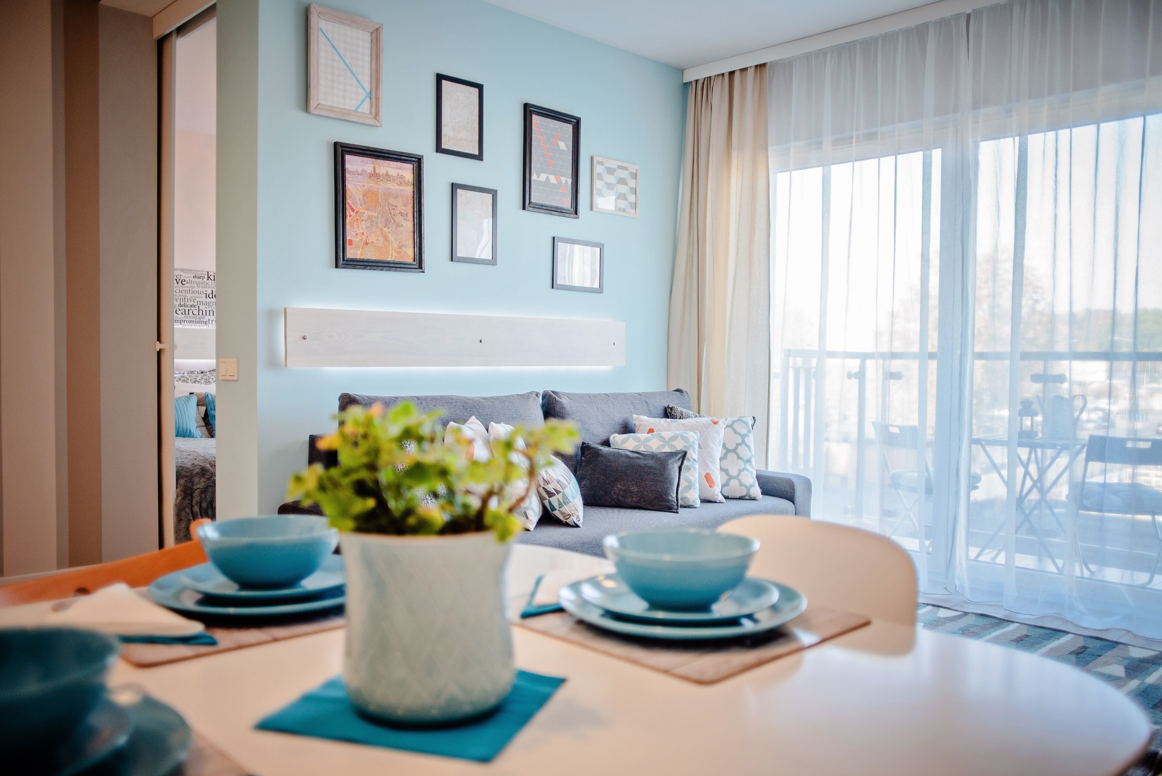 A modern living room with a sofa, a dining table with blue bowls, and a potted plant.