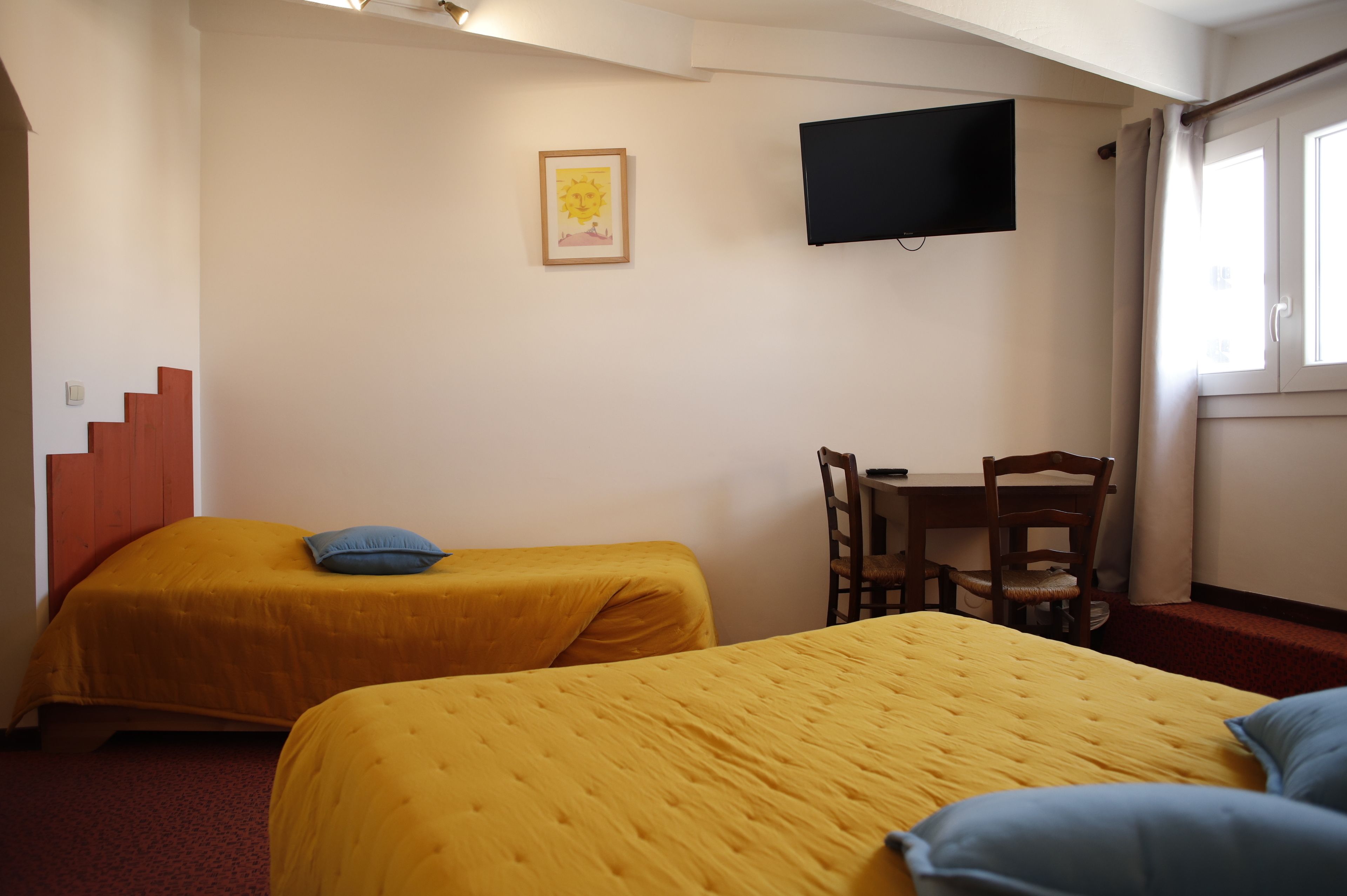 Une chambre d’hôtel avec deux lits, un bureau, une chaise, une télévision et une fenêtre avec des rideaux.