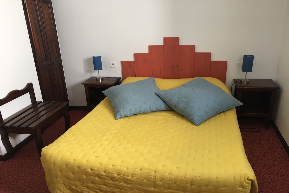 A hotel room with a bed, two bedside tables, a chair, and a wooden headboard.
