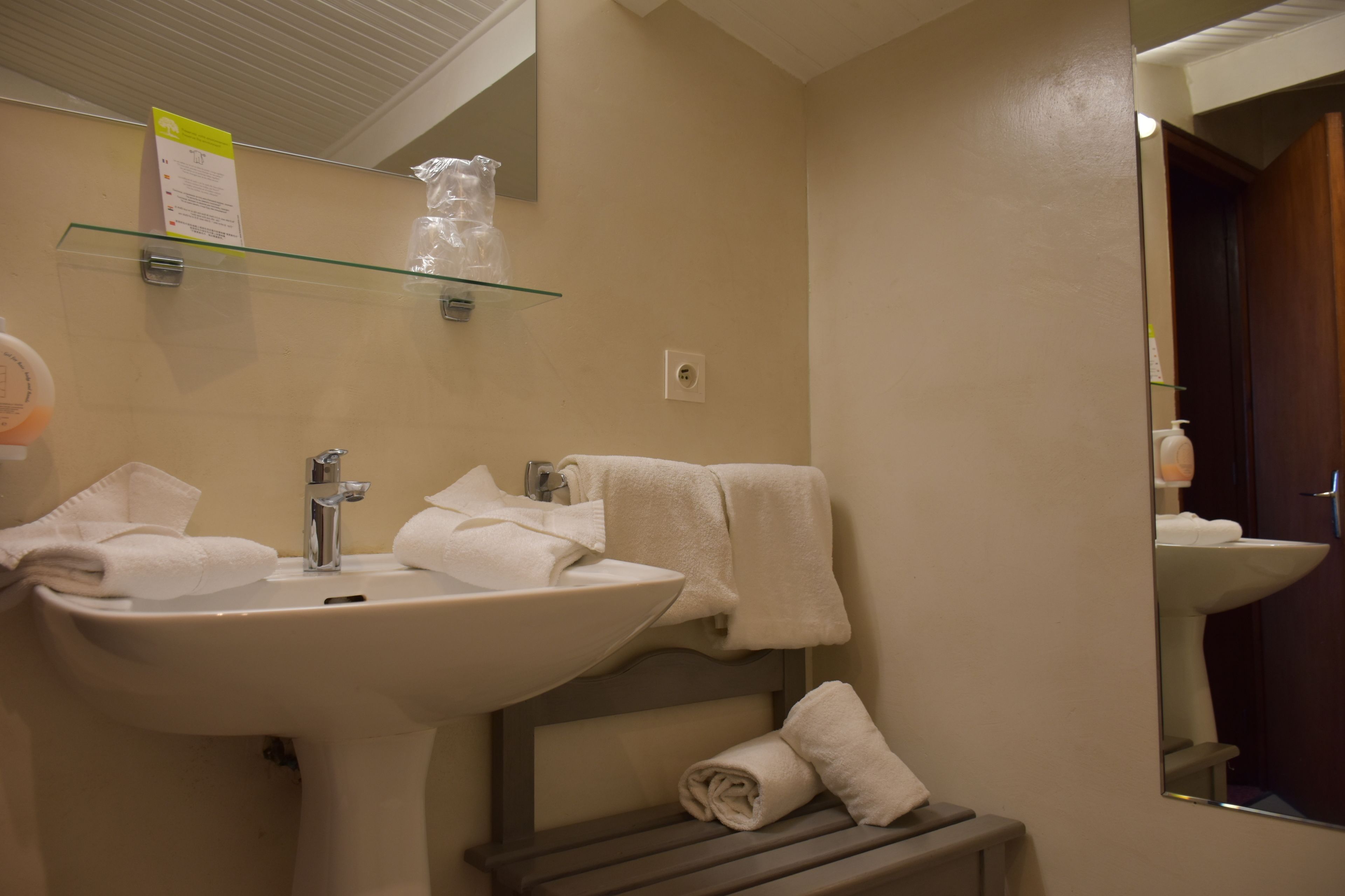 A bathroom with a sink, mirror, towel rack, and a glass shelf with toiletries.