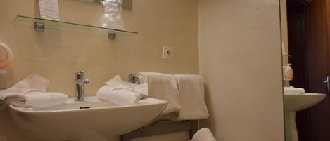 A bathroom with a sink, mirror, towel rack, and a glass shelf with toiletries.