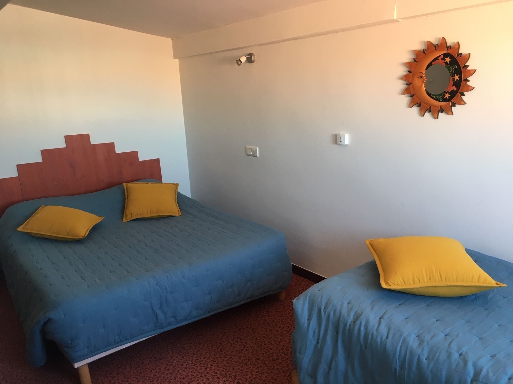 A room with a bed, two pillows, a wall-mounted mirror, and a light fixture.