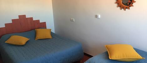 A room with a bed, two pillows, a wall-mounted mirror, and a light fixture.