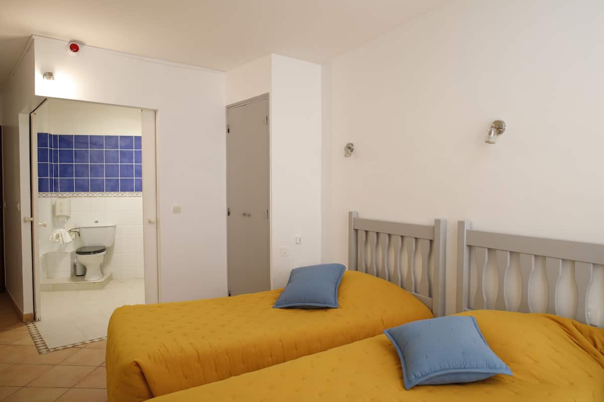 A hotel room with two beds, a bathroom, and a door leading to another room.