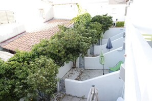 A narrow courtyard with a tiled roof, a tree-lined path, and a white wall with a small door. - Hôtel Le Fangassier (Saintes-Maries-de-la-Mer)