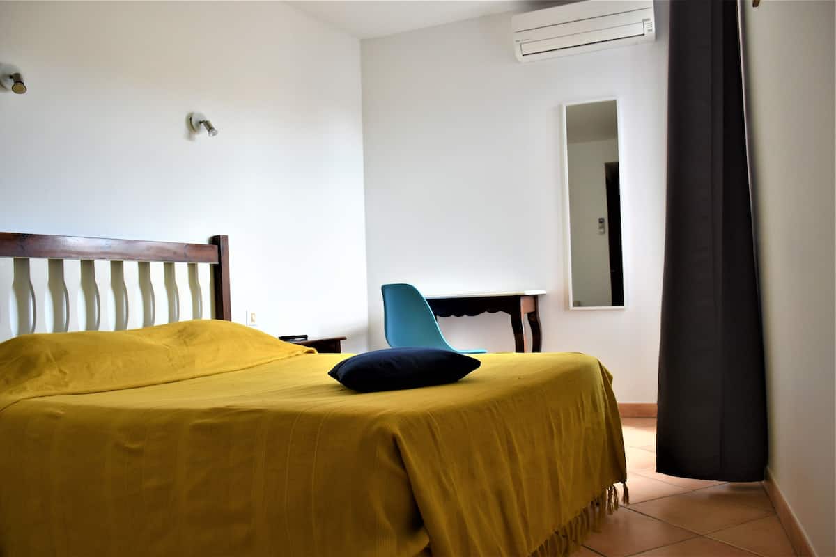 A room with a bed, a chair, a desk, and an air conditioning unit.