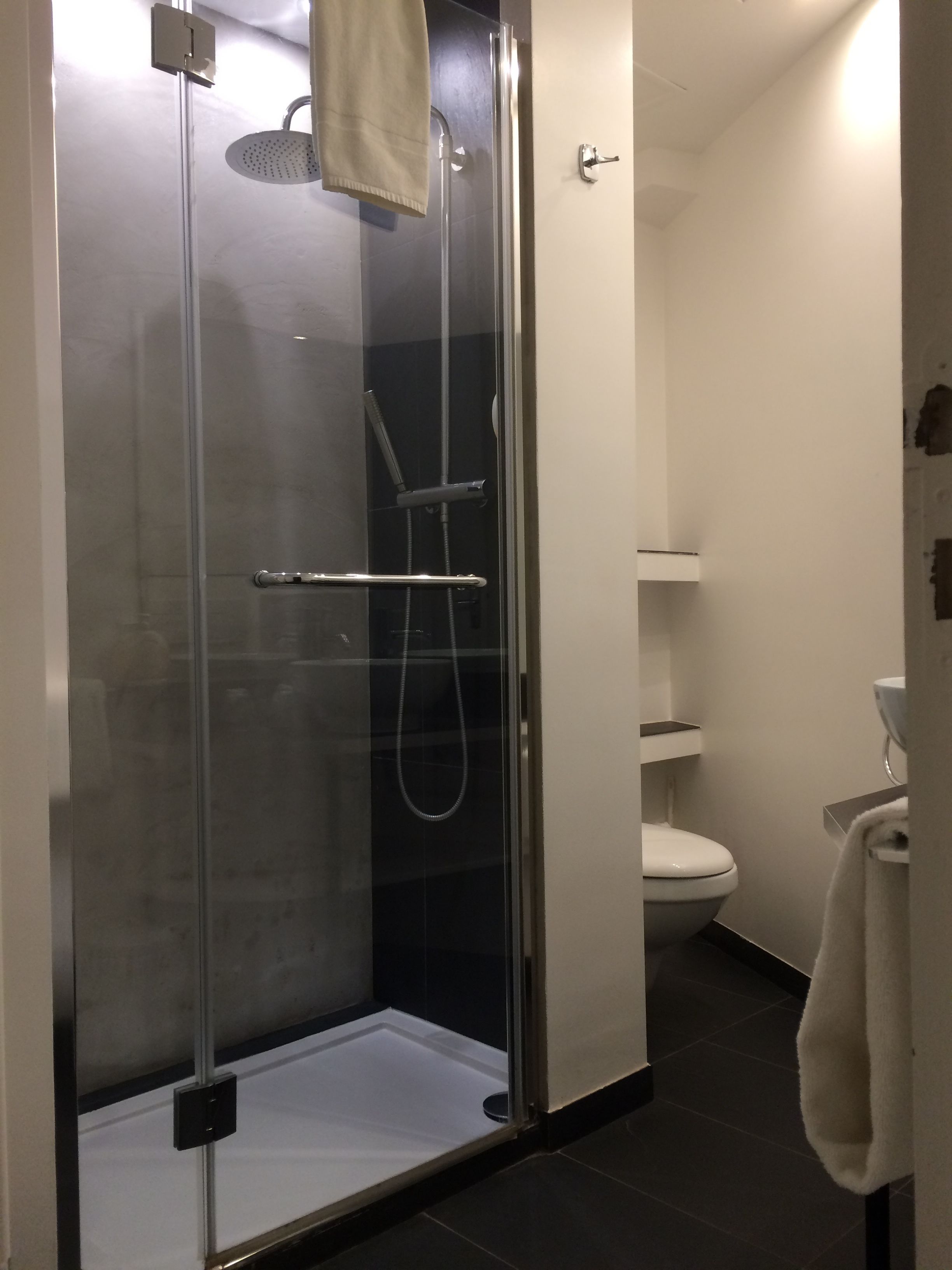 Ducha con cerramiento de vidrio, cabezal de ducha de mano y una toalla colgada en la puerta.