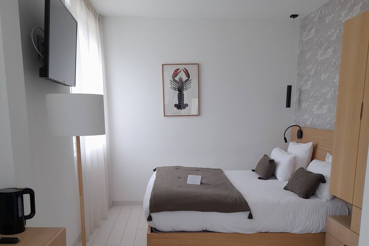 A modern hotel room with a bed, a desk, a chair, a television, and a framed picture on the wall.