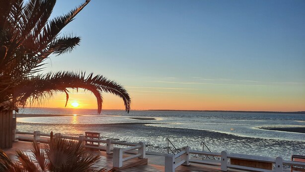 Una terraza de madera con barandilla que da a una playa al atardecer.