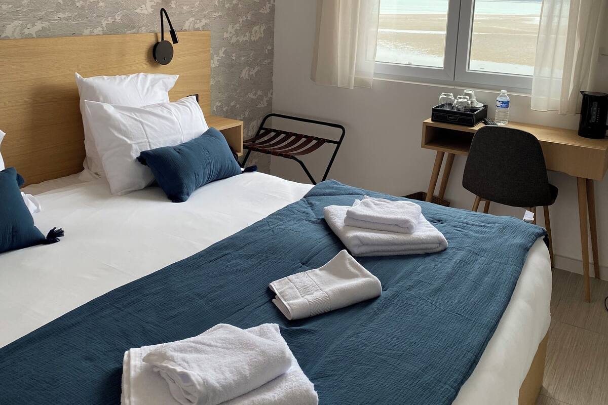 A hotel room with a bed, a desk, a chair, and a view of the beach.