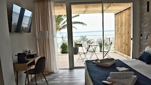 Habitación de hotel con cama, escritorio, silla y vista al mar a través de un ventanal corredero.