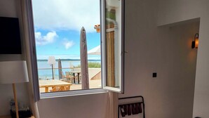 Habitación de hotel con cama, escritorio, silla, televisor y ventana con vista a la playa y al océano.