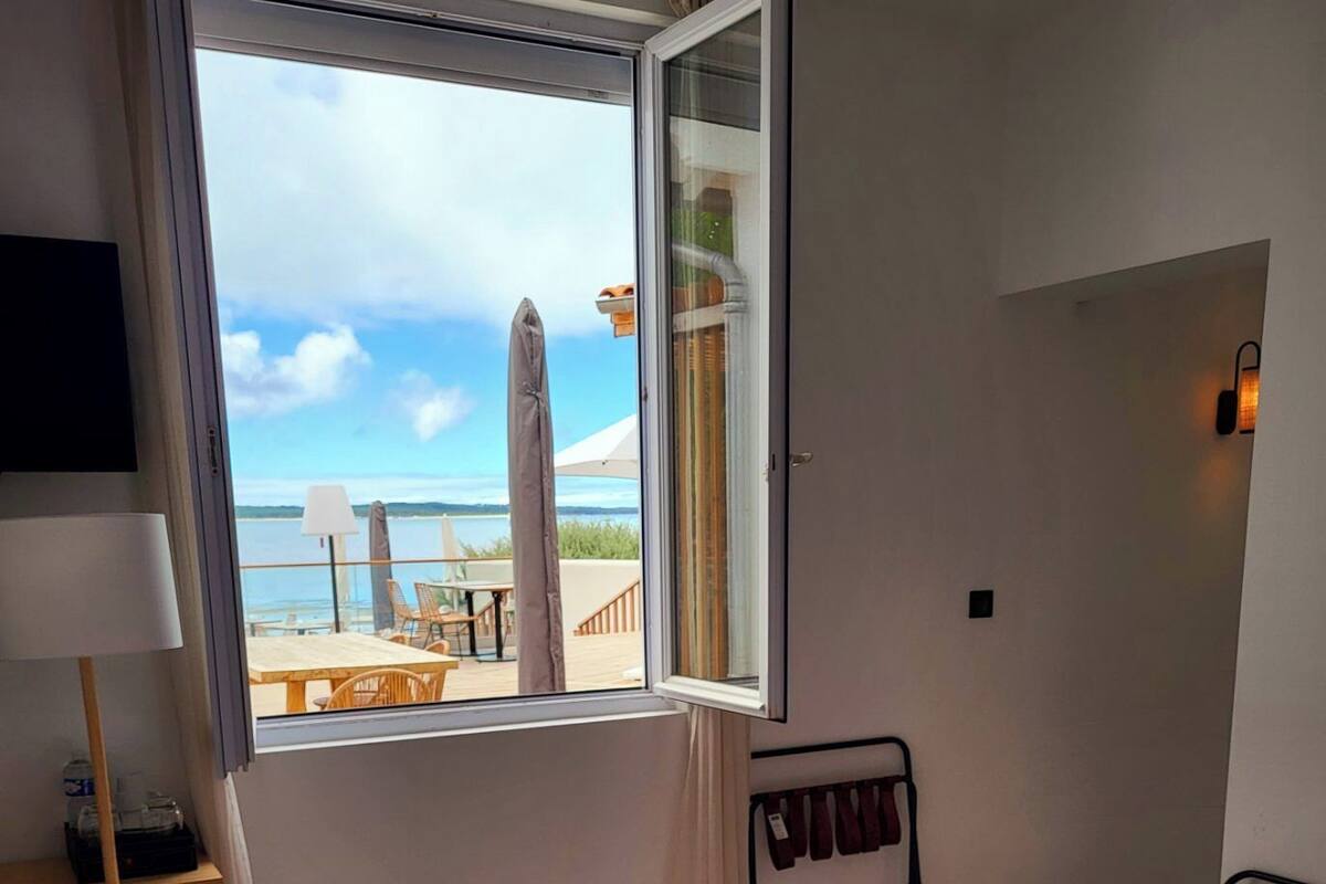 A hotel room with a bed, a desk, a chair, a TV, and a window with a view of the beach and ocean.