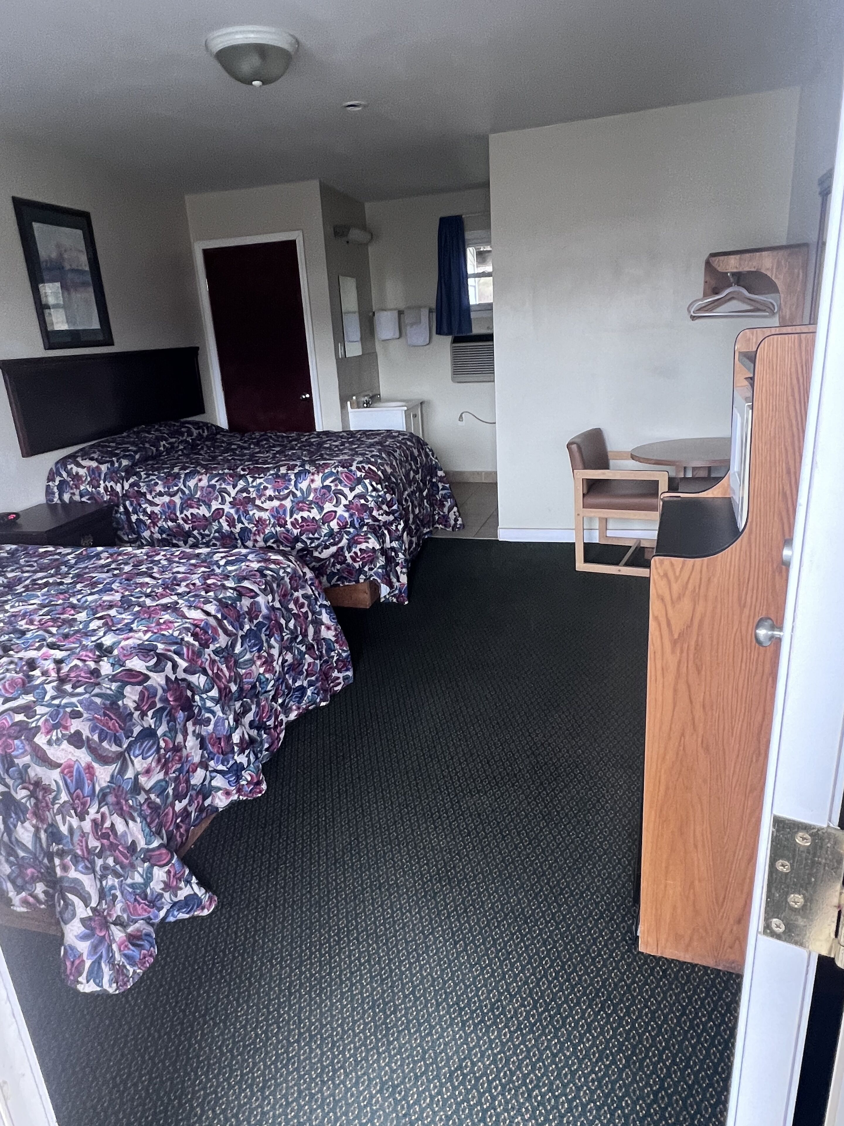 Habitación de hotel con dos camas, un escritorio pequeño, una silla, un espejo y una ventana con cortinas.