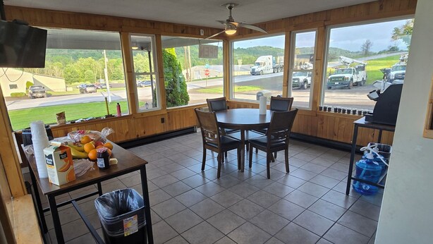 Comedor con mesa y sillas, un basurero y un ventanal con vista a un estacionamiento y camiones.