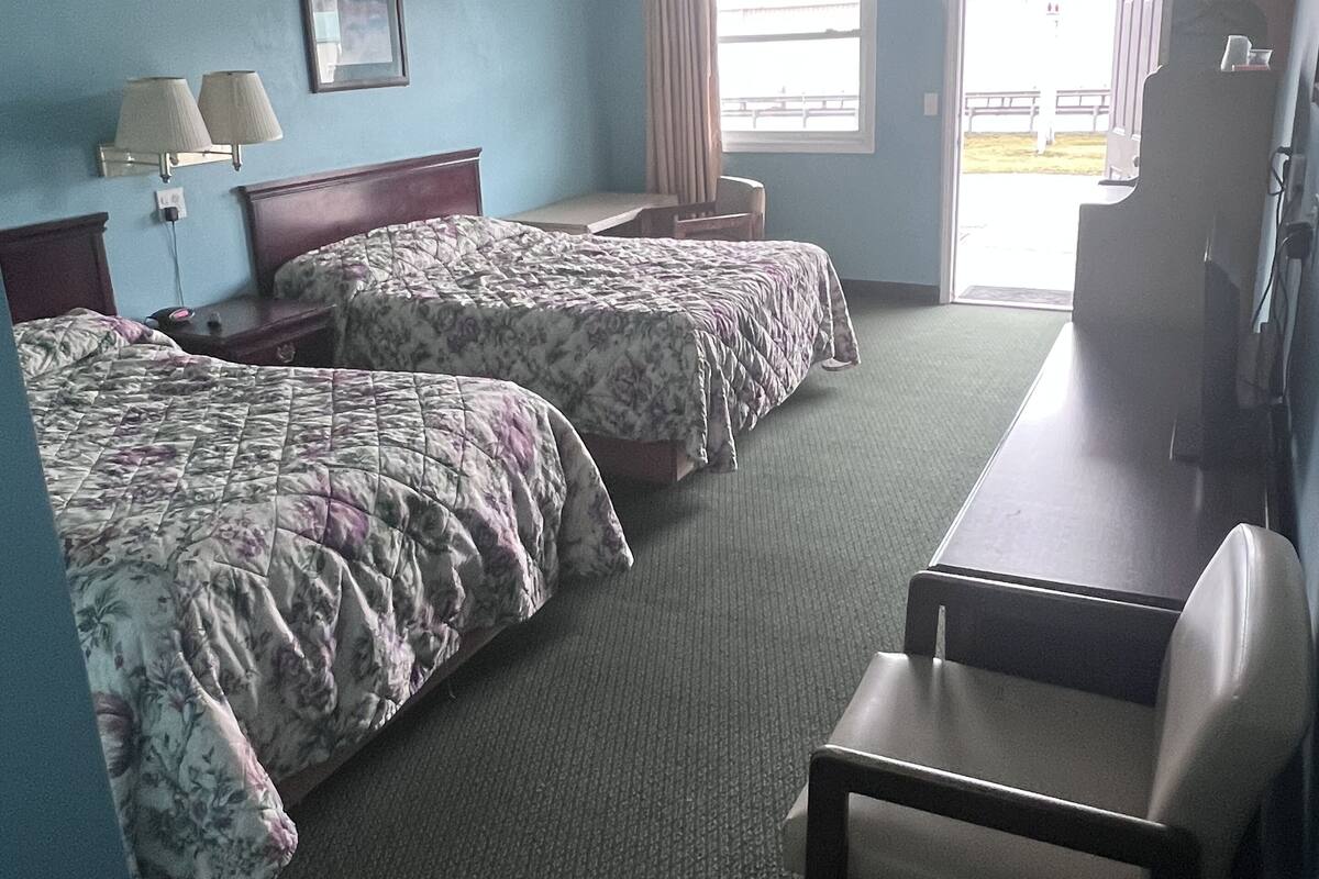 A hotel room with two beds, a desk, a chair, a lamp, and a window.