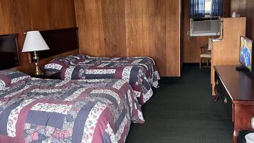 A hotel room with two beds, a desk, a TV, and an air conditioning unit.