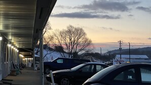 Un motel con zona de estacionamiento techada, una hilera de habitaciones con ventanas y vista al atardecer sobre un paisaje montañoso.