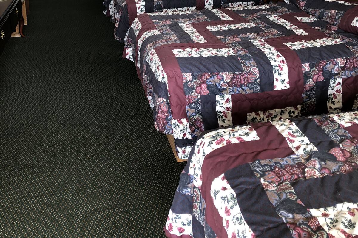 A hotel room with four beds, a TV, a desk, and a window with blinds.