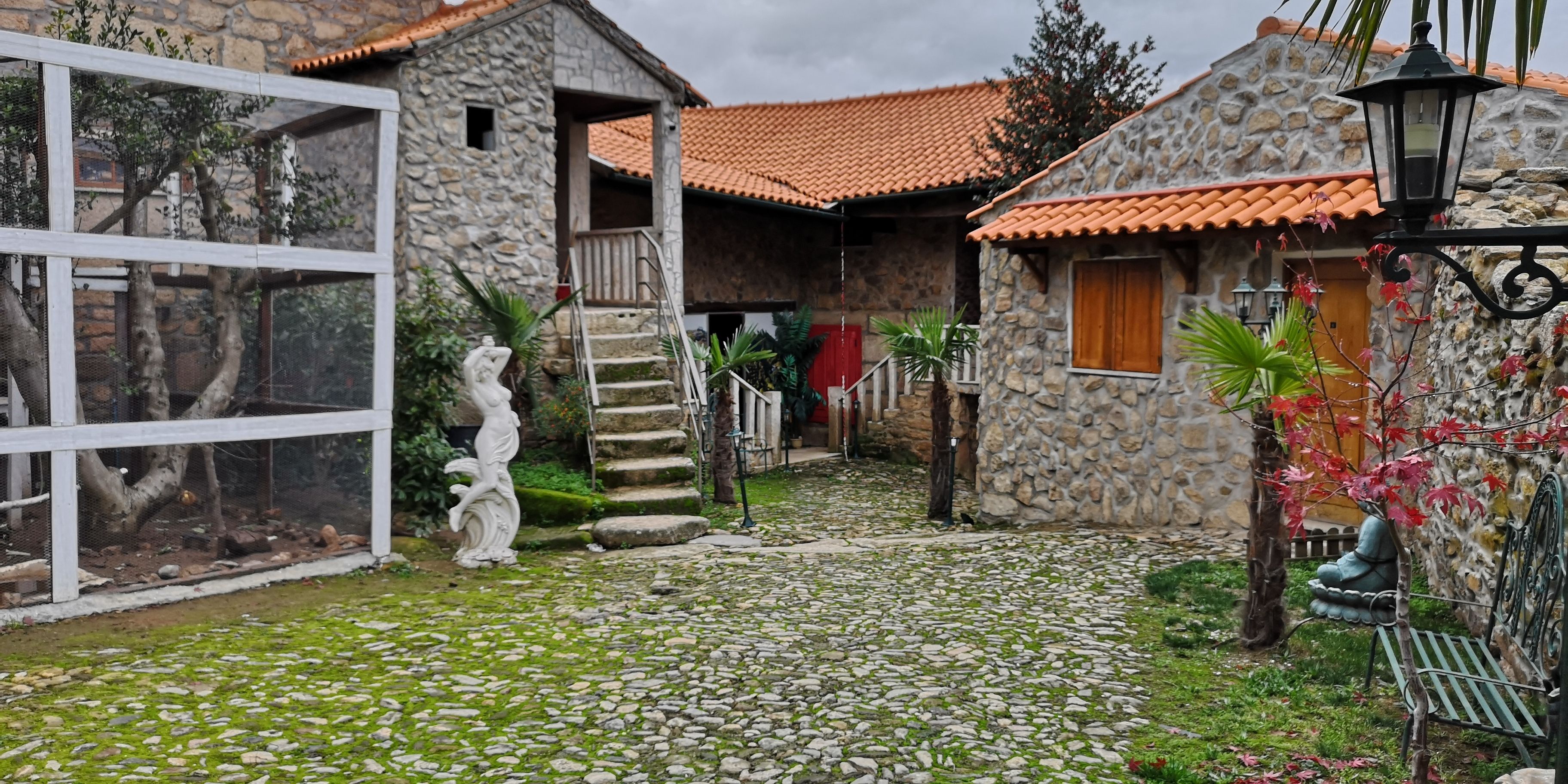 A courtyard with stone buildings, a statue, and a cobblestone path.