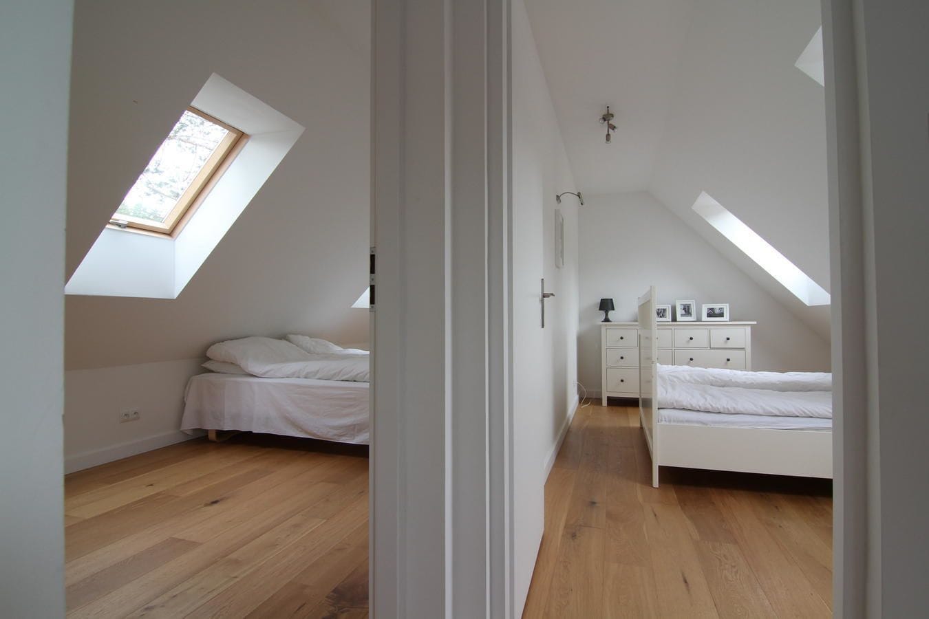 A bedroom with a sloped ceiling, a skylight, a bed, a dresser, and a nightstand.