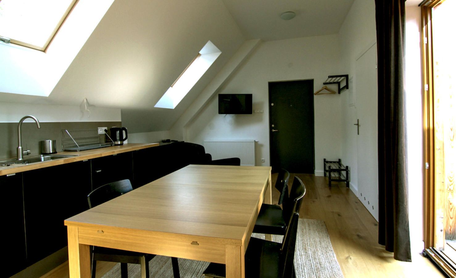 A compact kitchen with a wooden table and chairs, a built-in oven, and a window with a view of the outside.